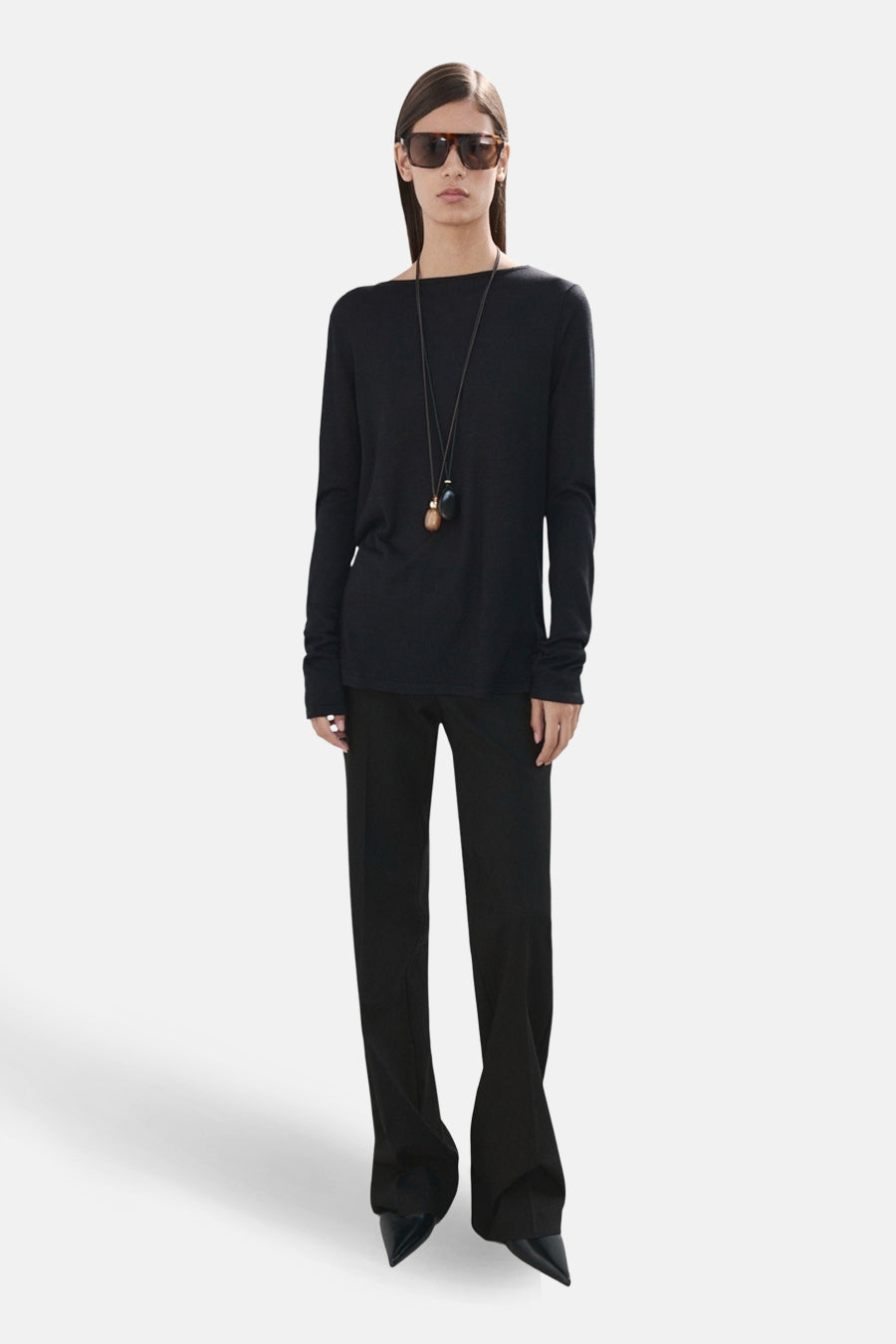 Zwarte trui met ronde hals van MANGO, met lange mouwen en gedragen met een lange ketting en een zwarte broek.