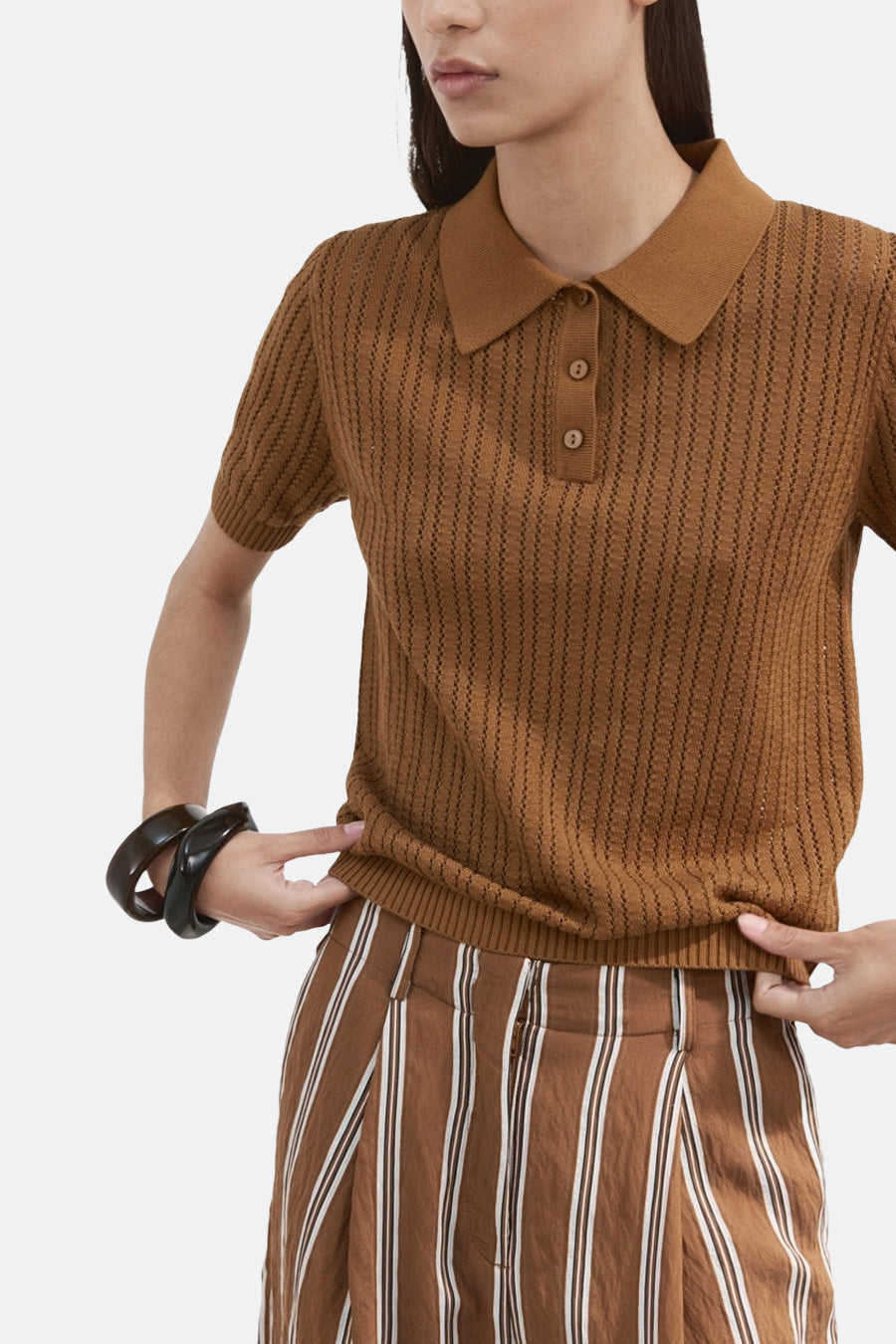 Polo marron de MANGO, à manches courtes, fermeture à boutons et côtes verticales, combinée avec un pantalon rayé.