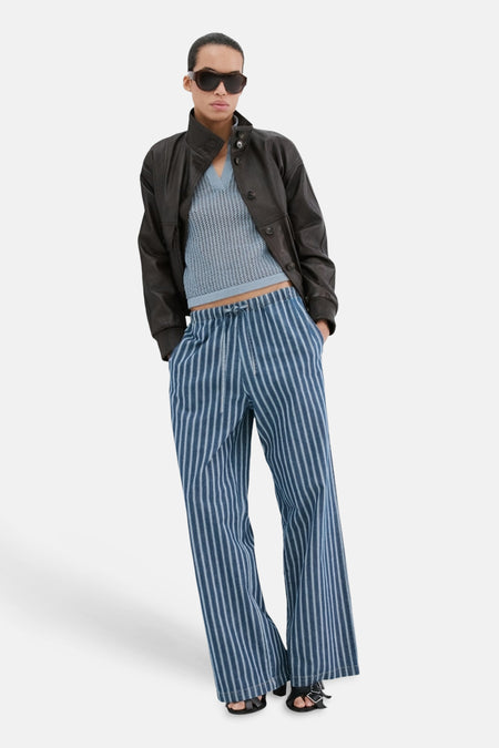 Blauwe polo met korte mouwen van MANGO, getextureerd en gecombineerd met een leren jas en gestreepte broek.