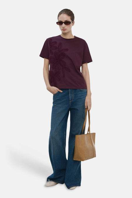 T-shirt Bordeaux de MANGO, avec motif floral sur le devant, combiné avec un jean ample et un sac marron.
