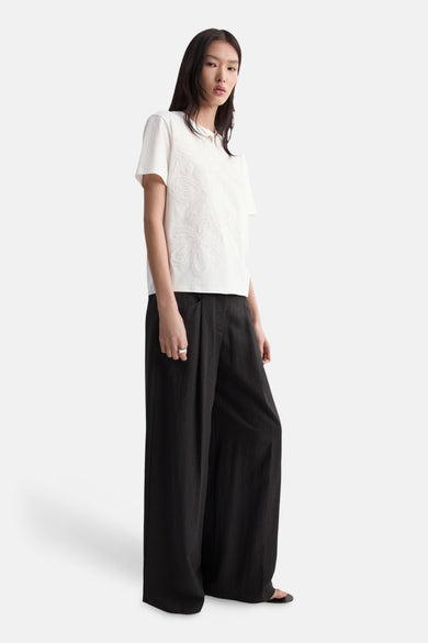 Wit T-shirt van MANGO met korte mouwen, voorzien van subtiele bloemdetails aan de voorkant. Gedragen met zwarte, wijde broek.