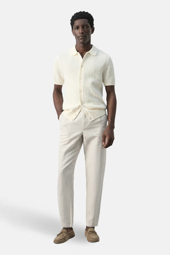 Ecru broek van MANGO, gecombineerd met een lichtgekleurd gebreid poloshirt en bruine mocassins.

