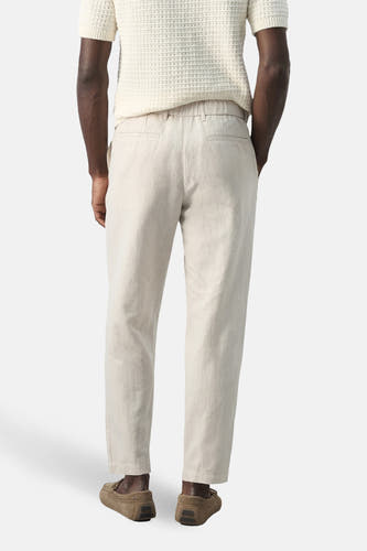 Ecru broek van MANGO, gezien van achteren, met een elastische tailleband en bruine instappers.
