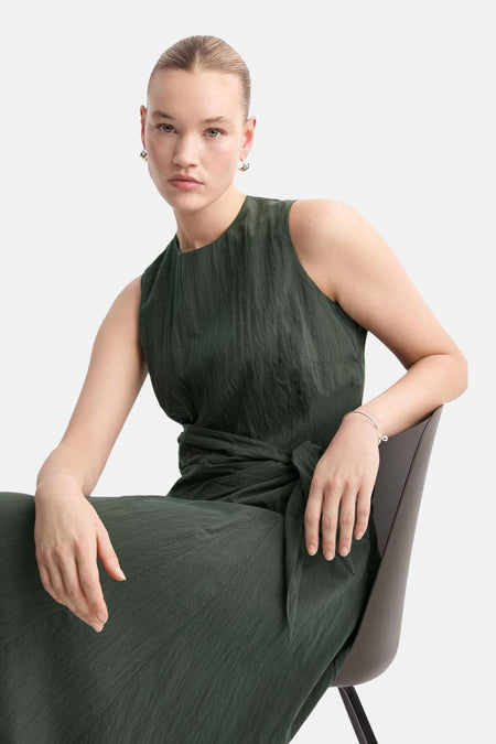 Robe kaki sans manches de MANGO avec texture tissée et ceinture à nouer, portée par un mannequin assis.