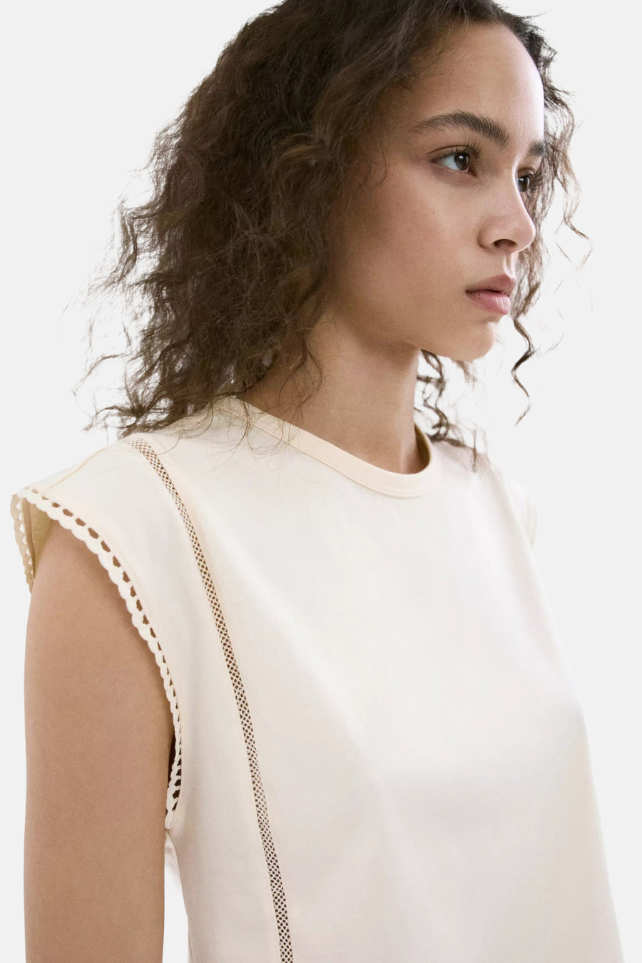 Beige mouwloze top van MANGO met kantdetails aan de schouders en zijkant, zijprofiel van model met krullend haar