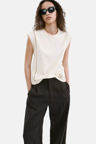 Beige mouwloze top van MANGO met geraffelde schouderdetails en knoopdetail aan de zijkant, gedragen met zwarte broek en zonnebril.