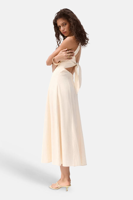 Beige korte mouwen jurk van MANGO, zijprofiel met open rug en strikdetail, gladde stof, model draagt gouden sieraden en sandalen
