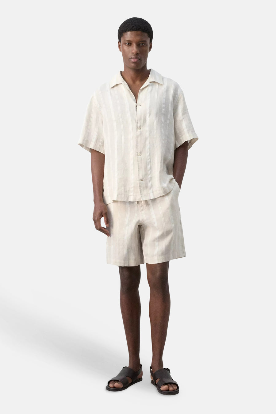Beige overhemd met korte mouwen van MANGO met verticale strepen, gedragen door een model met een bijpassende gestreepte short en donkere sandalen.