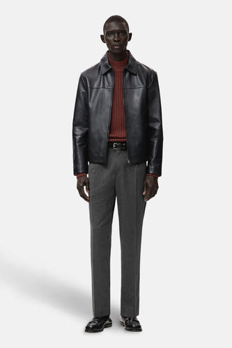 Pantalon gris de MANGO, associé à une veste brune, un manteau en cuir noir et des chaussures noires.