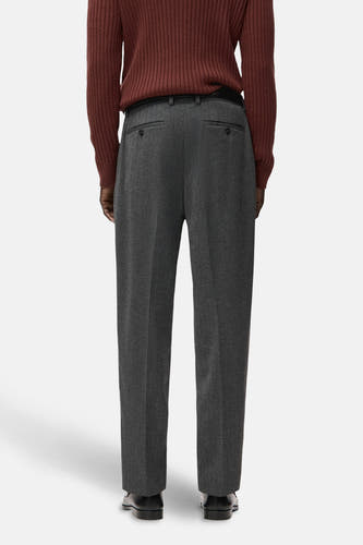 Grijze broek van MANGO, gezien van achteren, met een riem en gedragen met een roodbruine trui.