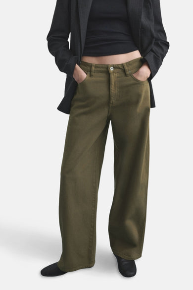 Kaki gekleurde jeans van MANGO, gedragen met een zwarte top en blazer, met handen in de zakken.

