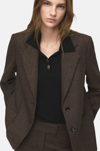 Pull-over noir à col rond de MANGO, avec une texture côtelée et des détails de boutons, porté sous un blazer marron à revers.