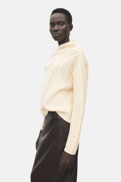 Veste écru avec col rond de MANGO, à motif côtelé et portée avec une longue jupe sombre.