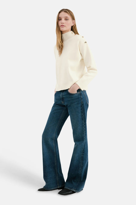 Pull col rond écru de MANGO, avec boutons dorés décoratifs sur les épaules, combiné avec un jean bleu à jambes larges.