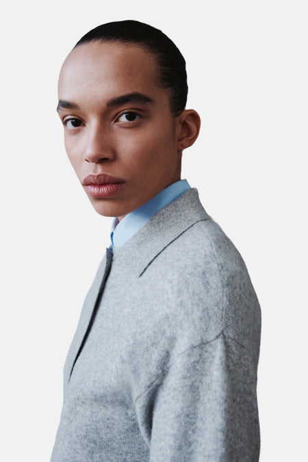 Model draagt grijze trui over blauw overhemd.