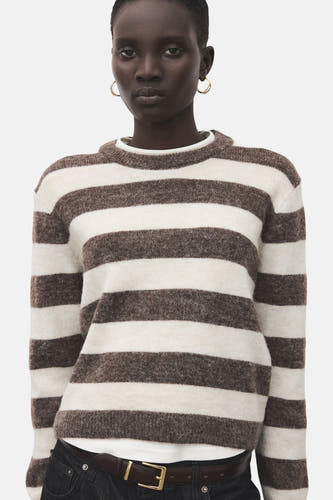 Sweat-shirt multicolore à col rond de MANGO, avec des rayures brunes et crème, associé à des jeans noirs et des baskets.