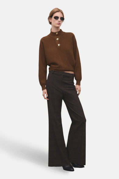 Bruine rolkraagtrui van MANGO, met lange mouwen en goudkleurige knopen op de hals, gecombineerd met een bruine pantalon.
