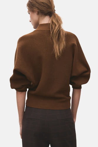 Bruine trui met rolkraag van MANGO, gebreide textuur en pofmouwen, met een geruite broek.
