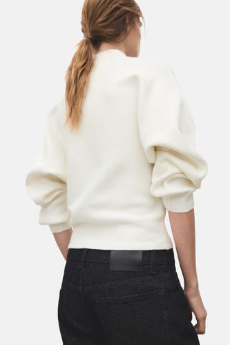 Ecrukleurige trui met rolkraag van MANGO, met lange pofmouwen en geribbelde textuur, gecombineerd met een donkere jeans.
