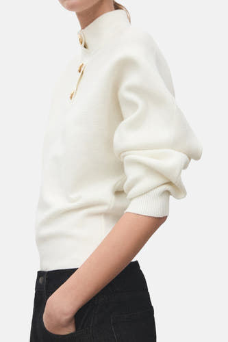T-shirt à col montant écru de MANGO, avec des manches longues et des boutons dorés, porté avec un pantalon noir, vue arrière.