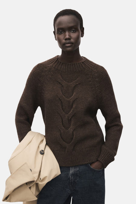 Bruine trui met ronde hals van MANGO, met kabelpatroon op de voorkant, gecombineerd met een beige jas en jeans.
