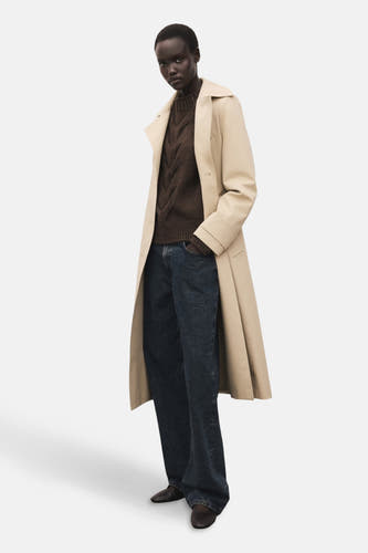 Bruine trui met ronde hals van MANGO, gedragen onder een beige trenchcoat met donkerblauwe wijde pijpen jeans.