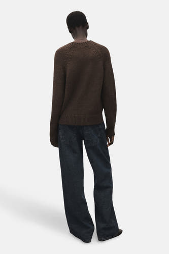 Bruine trui met ronde hals van MANGO, met raglanmouwen, gedragen met donkerblauwe jeans, gezien van achteren.
