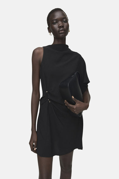 Zwarte mouwloze jurk van MANGO, met een asymmetrisch ontwerp en draperingen aan de zijkant, gecombineerd met een zwarte tas.