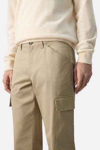 Beige broek van MANGO, met cargozakken en een knoopsluiting, gedragen met een crèmekleurige trui.
