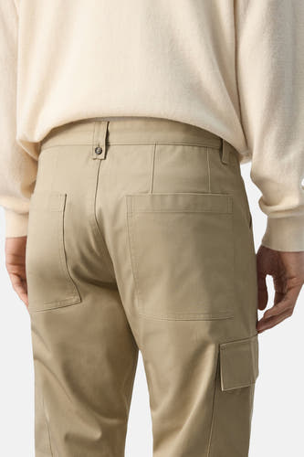 Beige broek van MANGO, met achterzakken en een cargo zak op het been, gezien van achteren.
