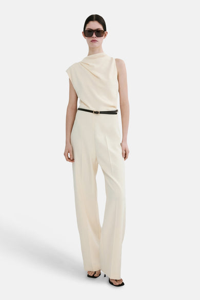 Ecru jumpsuit van MANGO, met een elegante drapering, een zwarte riem en wijde pijpen.

