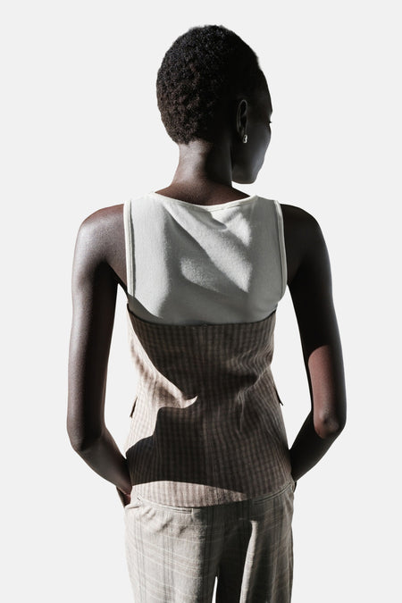 Grijze mouwloze blouse van MANGO, van achteren gezien, met ruitpatroon over een witte top en geruite broek.