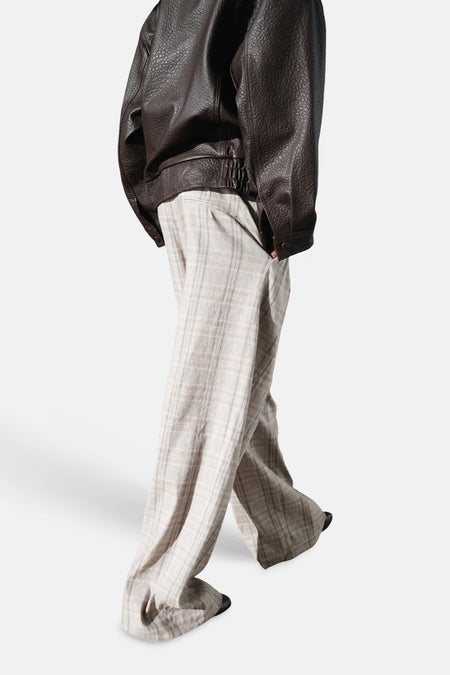 Pantalon beige de MANGO, à motif à carreaux et jambes larges, porté avec une veste en cuir marron.