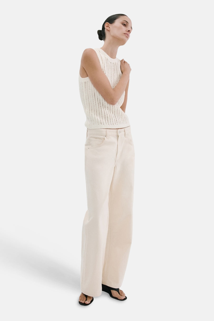 Mouwloze ecru top van MANGO, met open gebreide textuur, gecombineerd met wijde crèmekleurige jeans en sandalen.