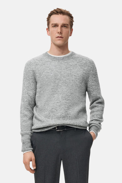 Sweat-shirt gris à col rond de MANGO, avec un motif subtil en maille fine, porté avec un pantalon foncé.