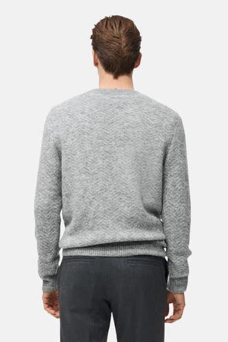 Grijze trui met ronde hals van MANGO, met een subtiel visgraatpatroon, gedragen met een donkere broek.
