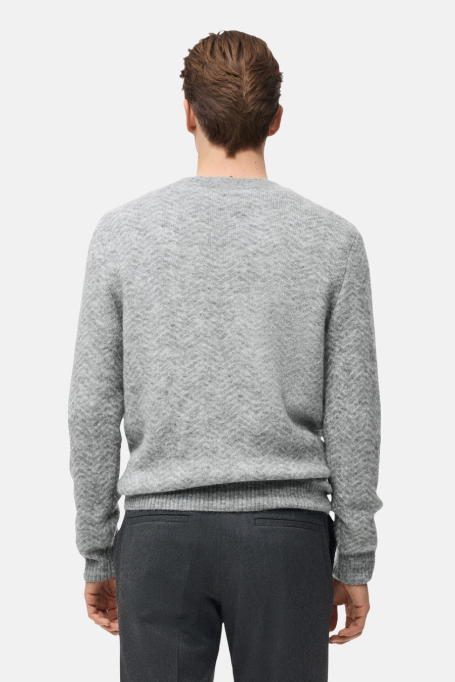 Grijze trui met ronde hals van MANGO, met een subtiel visgraatpatroon, gedragen met een donkere broek.
