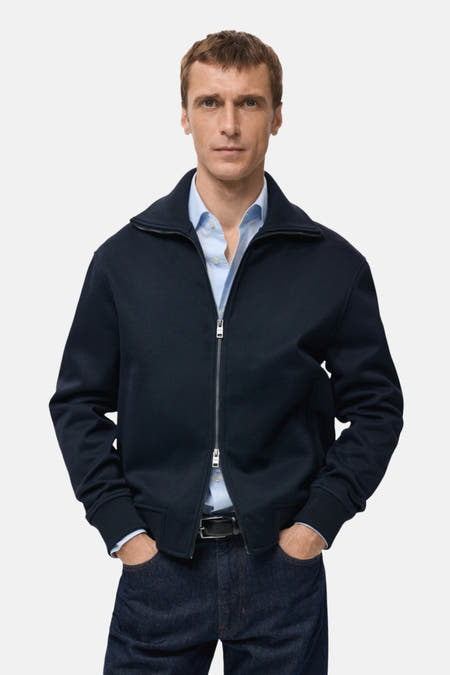 Blauw gilet van MANGO, gedragen over een lichtblauw overhemd en donkere jeans, met de handen in de zakken.
