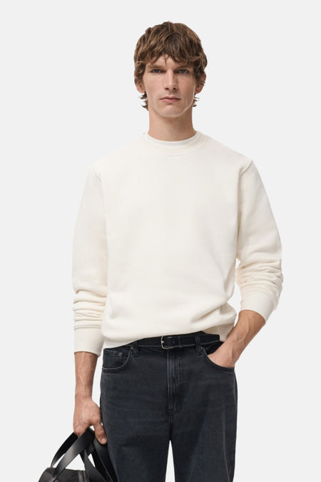 Man met crèmekleurige trui en donkere jeans.
