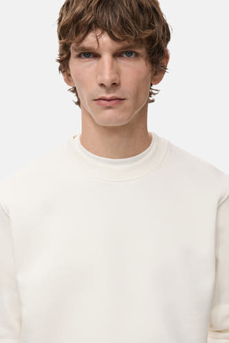 Pull-over blanc de MANGO, gros plan sur un modèle aux cheveux bruns et aux yeux bleus, contre un fond blanc.