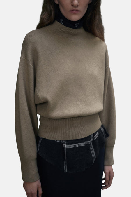 Vrouw draagt bruine trui met geruite blouse, staand.