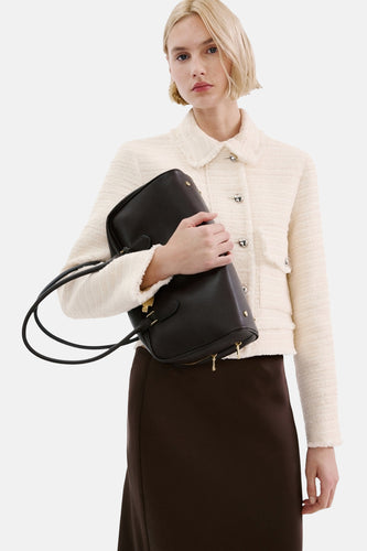 Vrouw in een crème jasje, bruine rok en zwarte handtas.