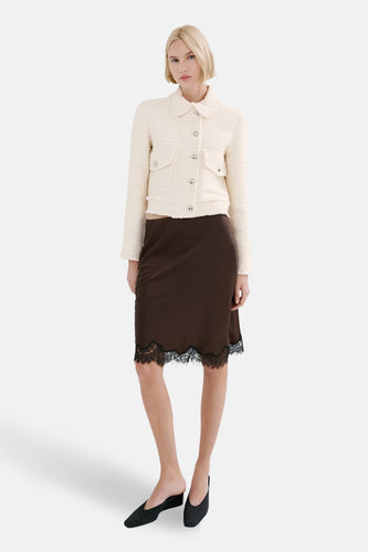 Model draagt crèmekleurig jasje en bruine rok met kant.