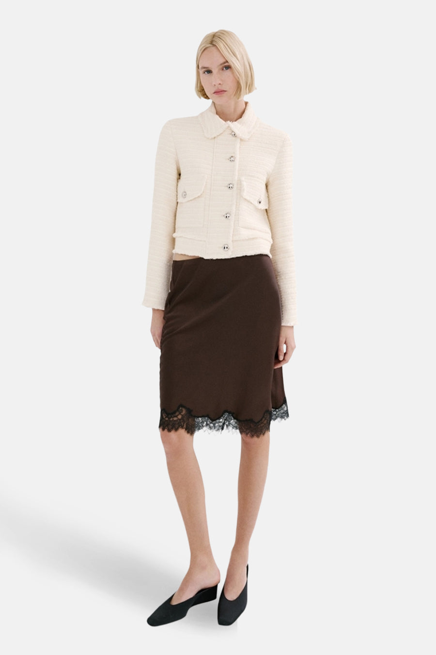 Model draagt crèmekleurig jasje en bruine rok met kant.