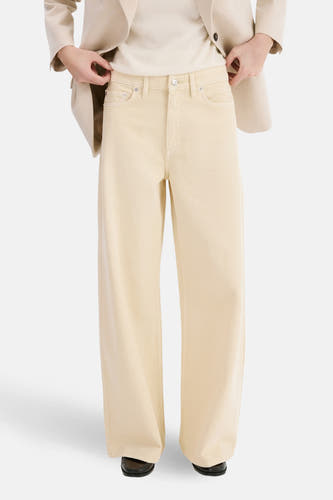 Jean de couleur beige de MANGO, avec jambes larges, poches arrière et un blazer de couleur claire.