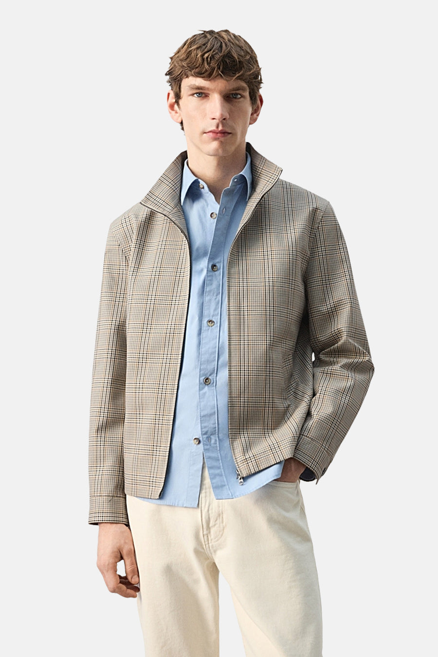 Multikleurige korte jas van MANGO, met een geruit patroon, gedragen over een lichtblauw overhemd en crèmekleurige broek.
