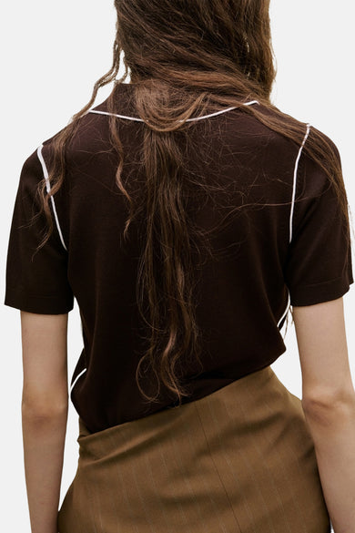 Polo marron à manches courtes de MANGO, fini avec des passepoils blancs le long des épaules et une jupe marron rayée.