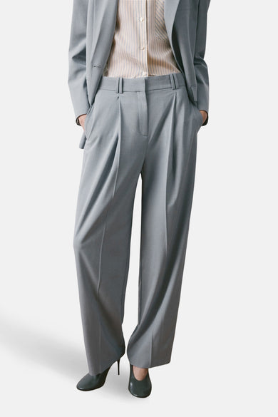 Pantalon de costume bleu de MANGO, vu de dos, avec une chemise rayée et des talons.