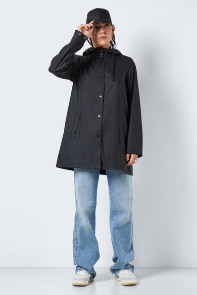 Zwarte regenjas van DROPLETS, met capuchon, lange mouwen, knoopsluiting en gedragen met een blauwe jeans en witte sneakers.