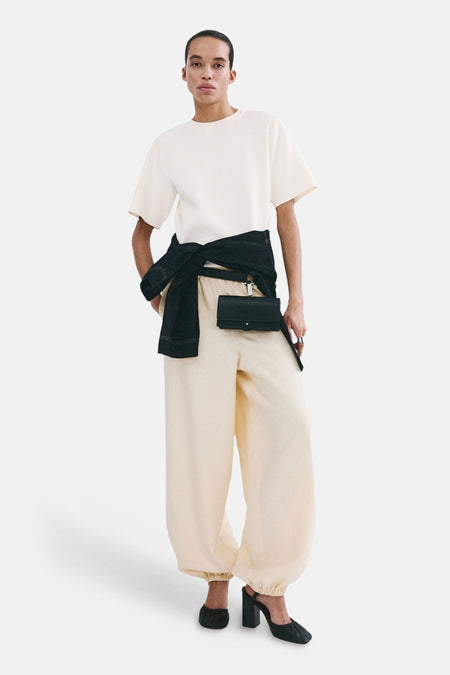 Pull écru à col rond de MANGO, stylisé avec un pantalon ample de couleur crème, une ceinture noire et des talons noirs.